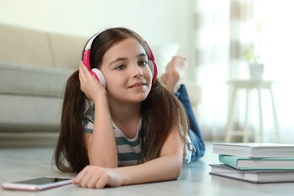 可爱的小女孩 带着耳机和智能手机在家里听有声读物 — 图库照片