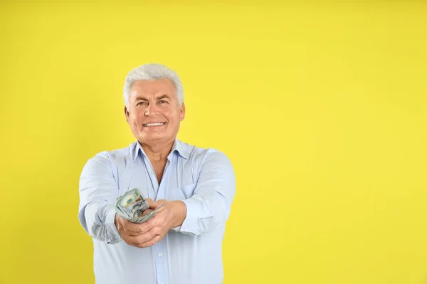 Happy senior man with cash money on yellow background. Space for text