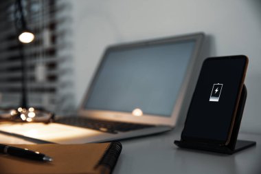 Masada kablosuz şarj aleti olan bir cep telefonu. Modern işyeri aksesuarı