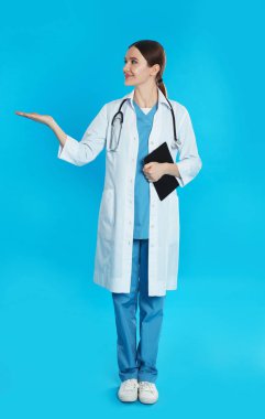 Mavi arka planda steteskopu ve panosu olan bir doktor.