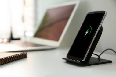 Beyaz masada kablosuz şarj aleti olan bir cep telefonu. Modern işyeri aksesuarı