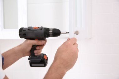 İşçi dolabın kapısına vida tabancası yerleştiriyor, yakın plan.