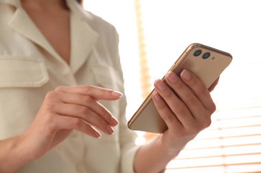 Modern akıllı telefonu kapalı mekanda kullanan genç bir kadın.