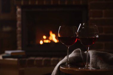 Şöminenin yanındaki ahşap masada kırmızı şarap kadehleri. Metin için boşluk