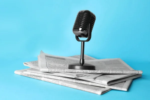 Newspapers and vintage microphone on light blue background. Journalist's work