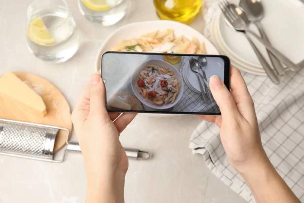 Food blogger taking picture of tasty pasta with shrimps and tomatoes at light table, closeup