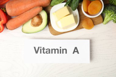Beyaz ahşap masa üzerinde A vitamini içeren farklı doğal besin ve kağıt.