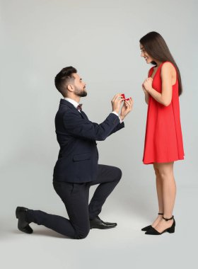 Nişan yüzüklü bir adam açık gri arka planda kız arkadaşına evlenme teklif ediyor.