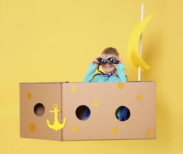 Małe Dziecko Bawiące Się Statkiem Kartonowego Pudełka Żółtym Tle — Zdjęcie stockowe