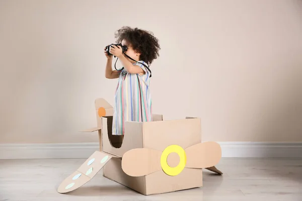 Cute African American child playing with cardboard plane and binoculars near beige wall