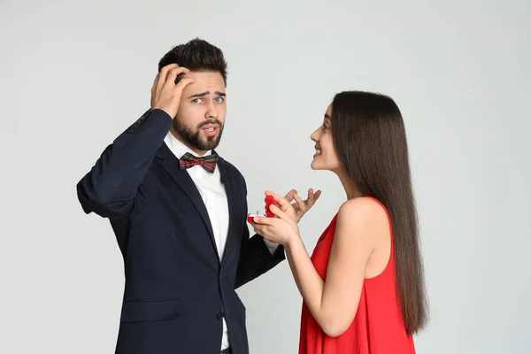 Young woman with engagement ring making marriage proposal to her boyfriend on light grey background