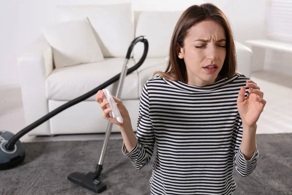 Young woman suffering from dust allergy while vacuuming house