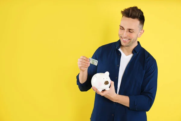 Happy Man Putting Money Piggybank Yellow Background Space Text — Stock Photo, Image