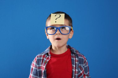 Mavi arka planda soru işareti olan duygusal küçük çocuk.