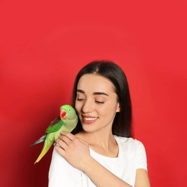 Kırmızı arka planda Alexandrine muhabbet kuşu olan genç bir kadın. Sevimli hayvan.