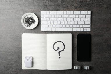 Soru işaretli defter, akıllı telefon ve klavye gri masada, düz konum