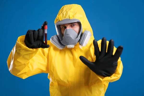 青色の背景に血液サンプルの試験管を保持する化学保護スーツの男 ウイルス研究 — ストック写真