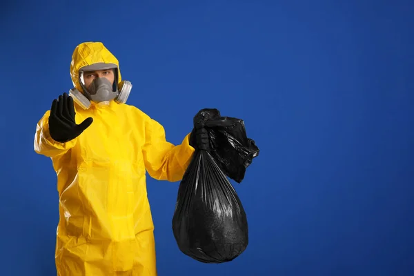 青い背景にゴミ袋を持っている化学防護服の男 テキストのためのスペース ウイルス研究 — ストック写真