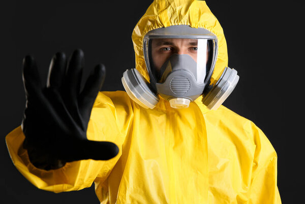 Man in chemical protective suit making stop gesture on black background. Virus research