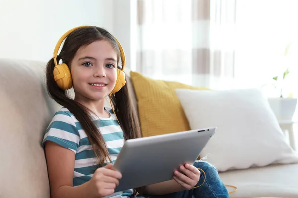 可爱的小女孩 带着耳机和平板电脑在家里听有声读物 — 图库照片
