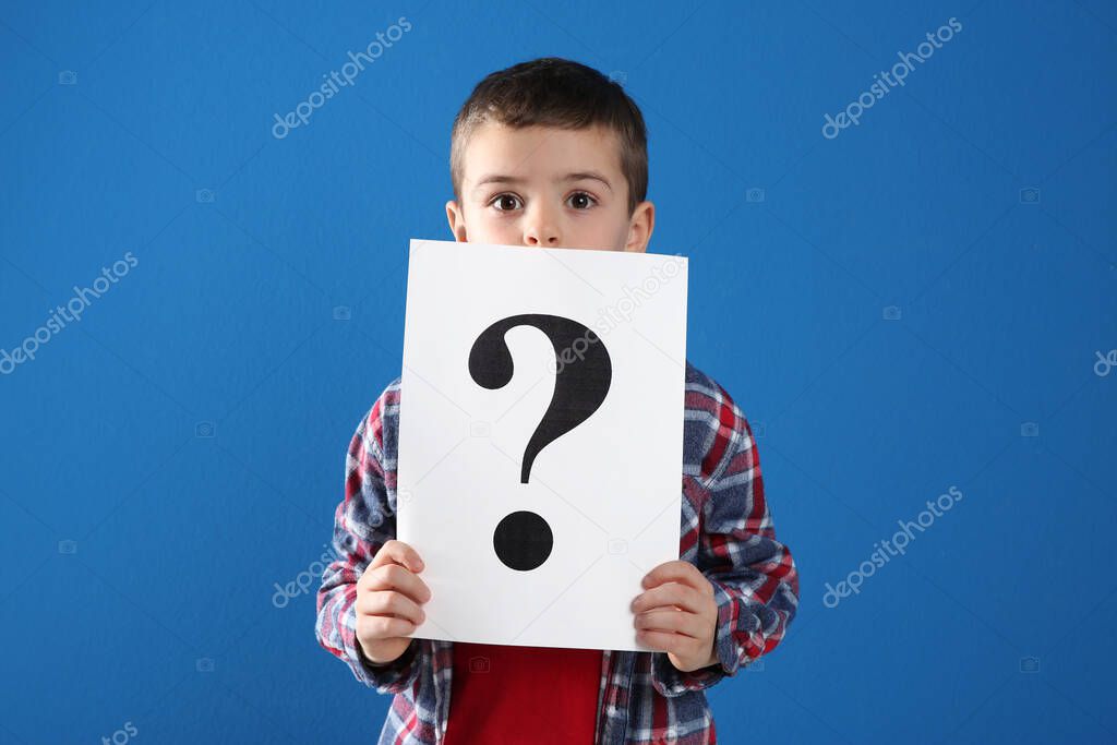 Emotional little boy holding paper with question mark on blue background