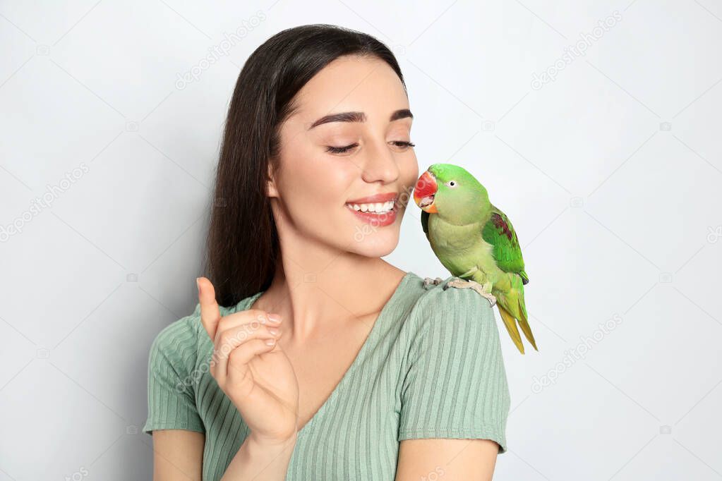 Young woman with Alexandrine parakeet on light background. Cute pet