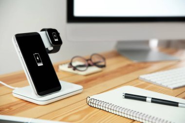 Cep telefonu ve ahşap masada kablosuz şarj aleti olan akıllı bir cihaz. Modern işyeri aksesuarı