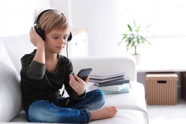 Kulaklıklı ve akıllı telefonlu şirin çocuk evde sesli kitap dinliyor.
