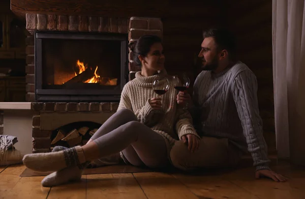 Lovely couple with glasses of wine near fireplace at home. Winter vacation