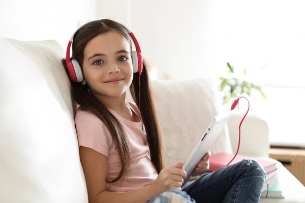可爱的小女孩 带着耳机和平板电脑在家里听有声读物 — 图库照片