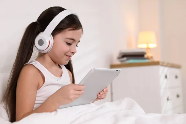 可爱的小女孩 带着耳机和平板电脑 在床上听有声读物 — 图库照片