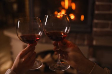 Yanan şöminenin yanında kırmızı şarap bardakları olan çift, yakın plan.