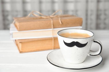 Kağıt bıyıklı bir kupa ve beyaz ahşap masada kitaplar. Babalar Günün kutlu olsun.