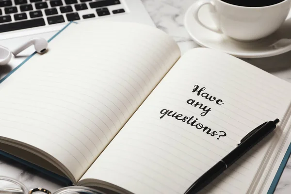 Notebook with phrase HAVE ANY QUESTIONS on white marble table, closeup