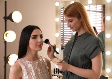 Profesyonel makyaj sanatçısı güzel bir kadınla kuaförde çalışıyor.