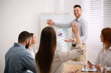 Genç bir kadın konferans odasında iş eğitiminde soru sormak için elini kaldırıyor.