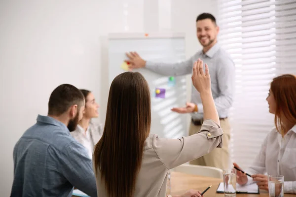 Young woman raising hand to ask question at business training in conference room