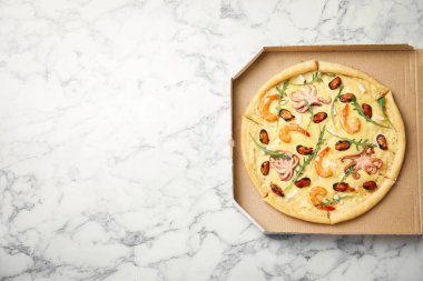 Beyaz mermer masanın üstünde karton kutuda nefis deniz ürünleri pizzası, üst manzara. Metin için boşluk