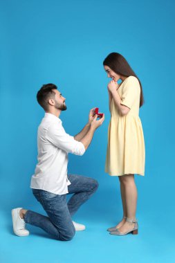 Nişan yüzüklü bir adam mavi arka planda kız arkadaşına evlenme teklif ediyor.