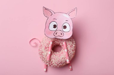 Donut ve pembe arka planda kağıt parçasından yapılmış komik bir domuz.