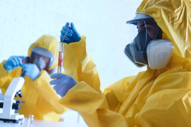 Kimyasal koruyucu kıyafetli bilim adamı laboratuardaki test tüpüne kan damlatıyor. Virüs araştırması