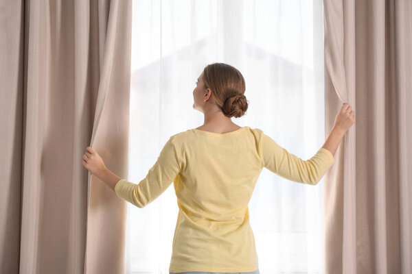 Woman opening window curtains at home in morning