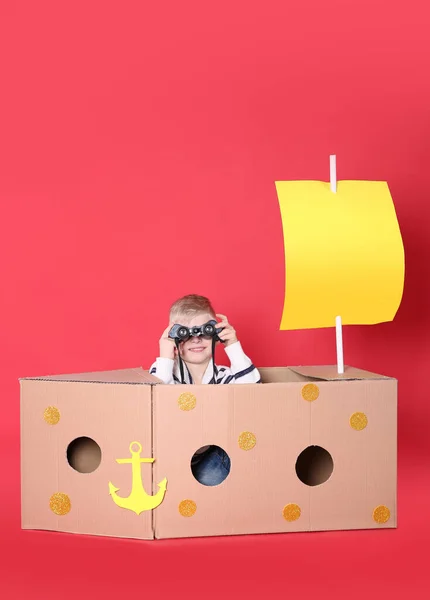 赤い背景に段ボール箱で作られた船で遊ぶ小さな子供 — ストック写真