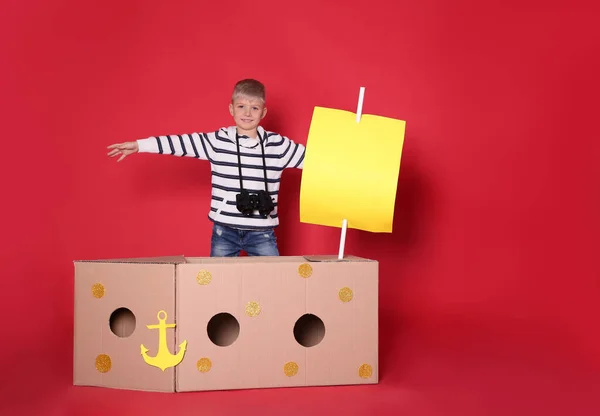 Kırmızı Arka Planda Karton Kutudan Yapılmış Gemiyle Oynayan Küçük Bir — Stok fotoğraf