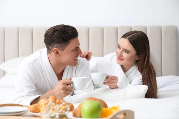 Happy couple in bathrobes with coffee on bed at home