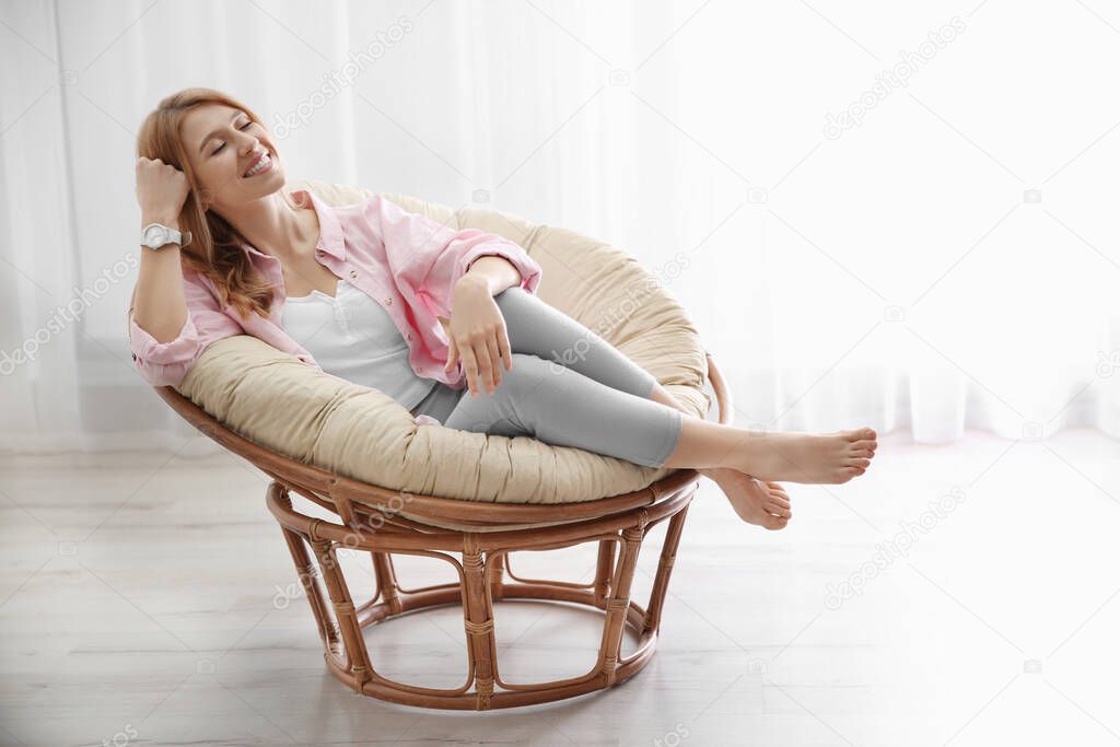 Young woman relaxing in papasan chair near window at home