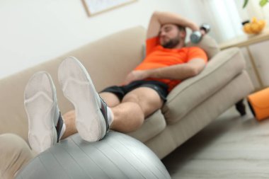 Evdeki kanepede spor aletleri olan tembel genç adam, bacaklarına odaklan.