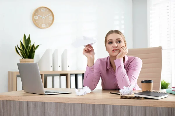 Lazy office worker playing with paper plane at desk indoors