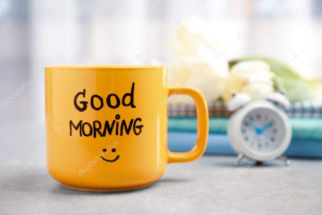 Cup of coffee with good morning wish on light grey table, closeup