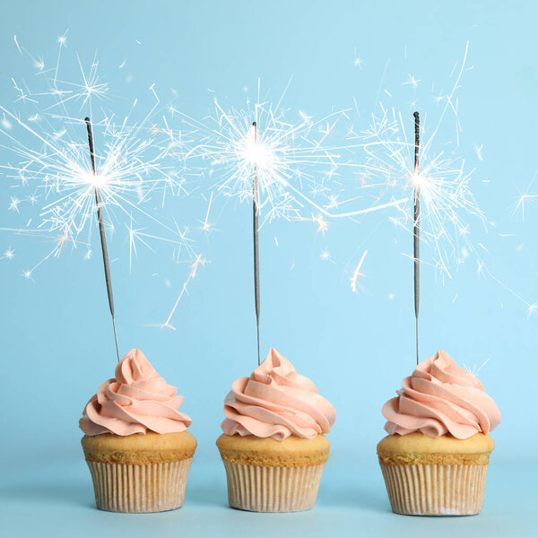 Birthday cupcakes with sparklers on light blue background